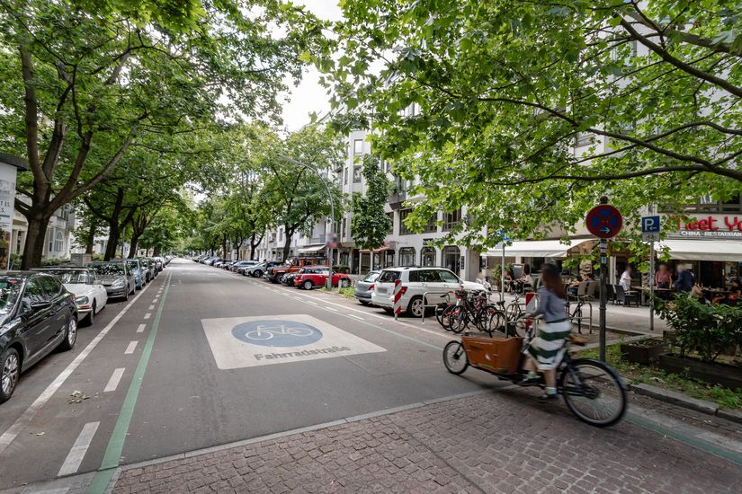 Radfahrerin mit einem Lastenrad auf einer markierten Fahrradstraße. Auf der rechten Fahrbahnrand sind Kreuzberger Bügel als Fahrradabstellanlagen angebracht.