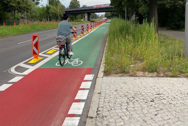 Radfahrerin auf einem mit Pollern geschützten Radweg. Der Radweg ist rot- und grünbeschichtet.