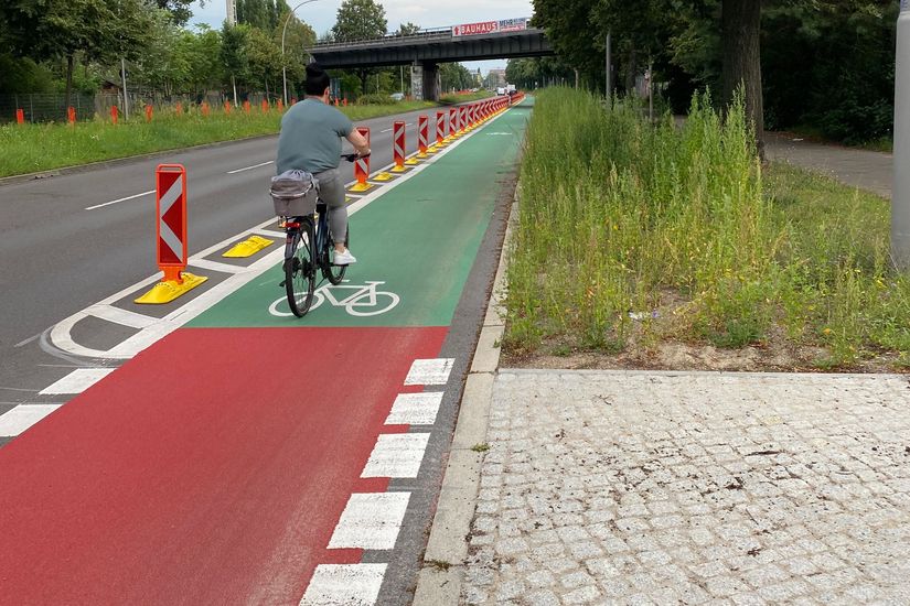 Radfahrerin auf einem mit Pollern geschützten Radweg. Der Radweg ist rot- und grünbeschichtet.