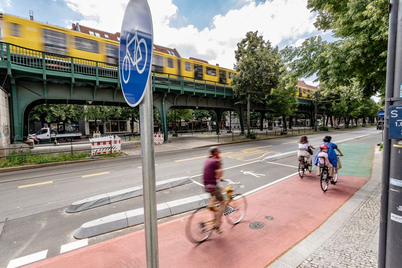 Radfahrer fahren auf einen geschützten Radfahrstreifen. Er ist farbig markiert. Im Hintergrund fährt die U-Bahn auf dem Viadukt der Schönhauser Allee.