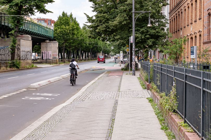 Radfahrer fährt auf dem geschützten Radfahrstreifen auf der Schönhauser Allee. Rechts auf dem Gehweg sieht man den ehemligen Hochbordradweg.