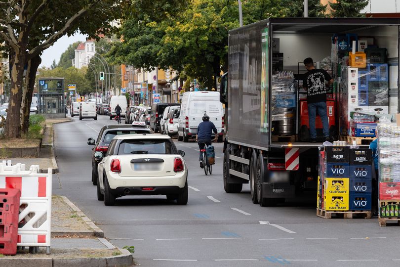 Vorher-Bild: Auf der Grunewaldstraße wird ein LKW ausgeladen. Es fahren Autos auf der Fahrbahn und ein Fahrradfahrer.