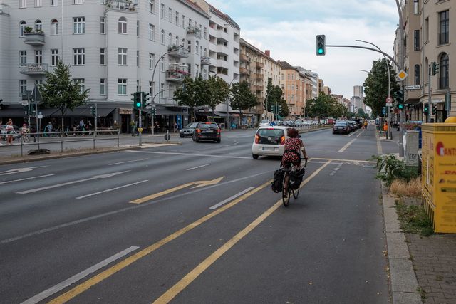 Gelbmarkierter Radfahrstreifen mit Sicherheitstrennstreifen. Radfahrerin fährt über die Kreuzung bei Grün.