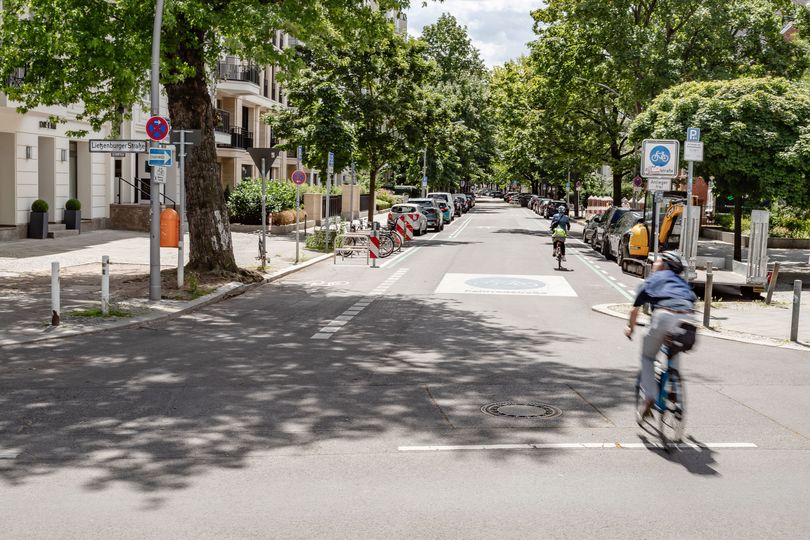 Zwei Radfahrende auf einer markierten Fahrradstraße. Am linken Fahrbahnrand sind Kreuzberger Bügel als Fahrradabstellplätze aufgestellt.