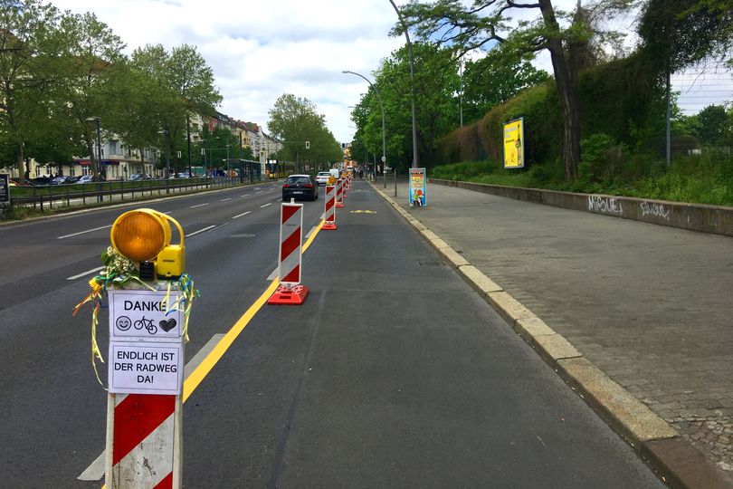 Temporärer Radfahrstreifen mit rot-weißen Leitbaken. Auf einem Schild steht: Danke! Endlich ist der Radweg da!