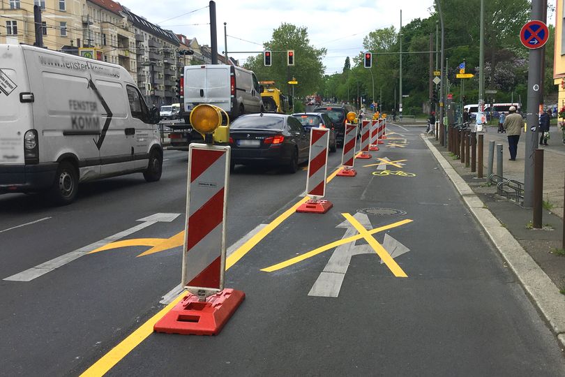 Temporärer Radfahrstreifen mit rot-weißen Leitbaken. Durchgestrichene Abbiegepfeile für den Autoverkehr.