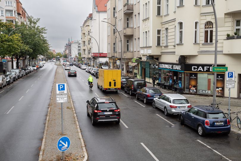 Vorher-Bild: Auf der Grunewaldstraße steht ein gelbes Post-Auto in zweiter Reihe. Weitere Autos und ein Fahrradfahrer fahren auf der Fahrbahn.